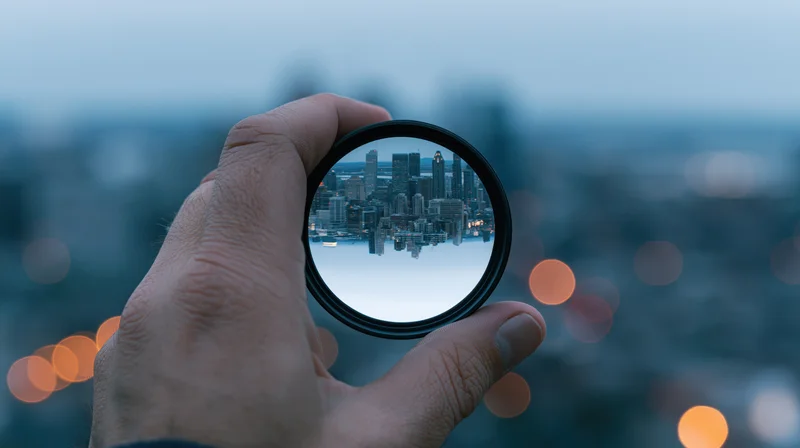 Hand holding a circular lens over a city skyline at twilight