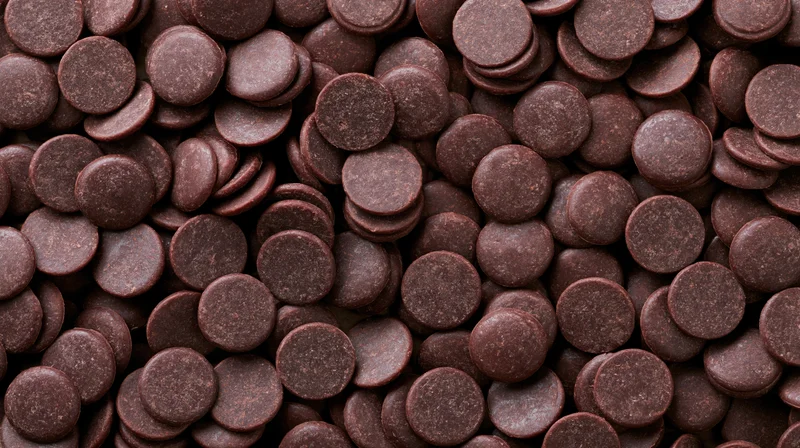 Closeup of dark chocolate couverture wafers scattered densely across the frame