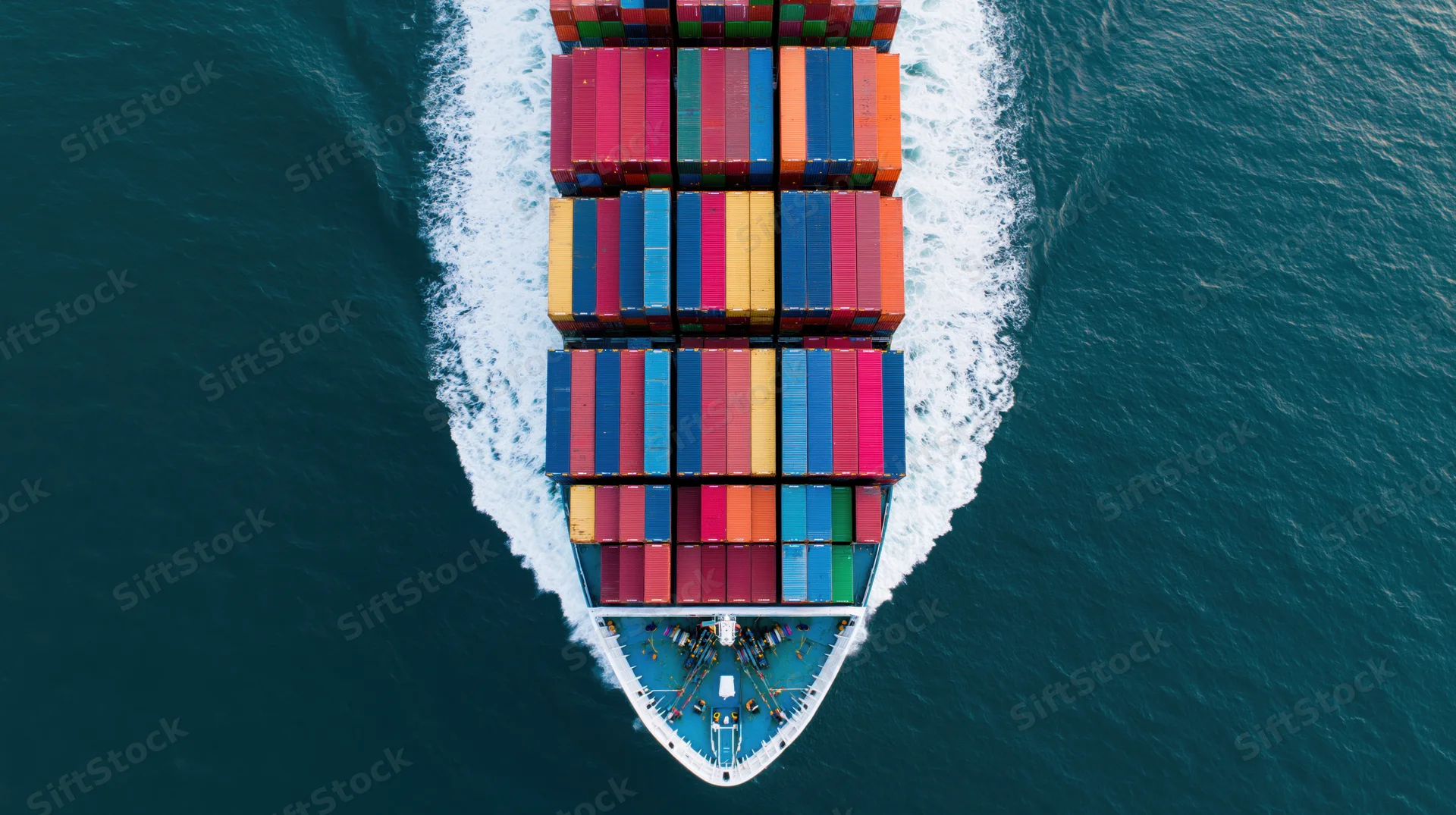 Overhead view of a cargo container ship moving through the ocean with stacked containers and a white wake