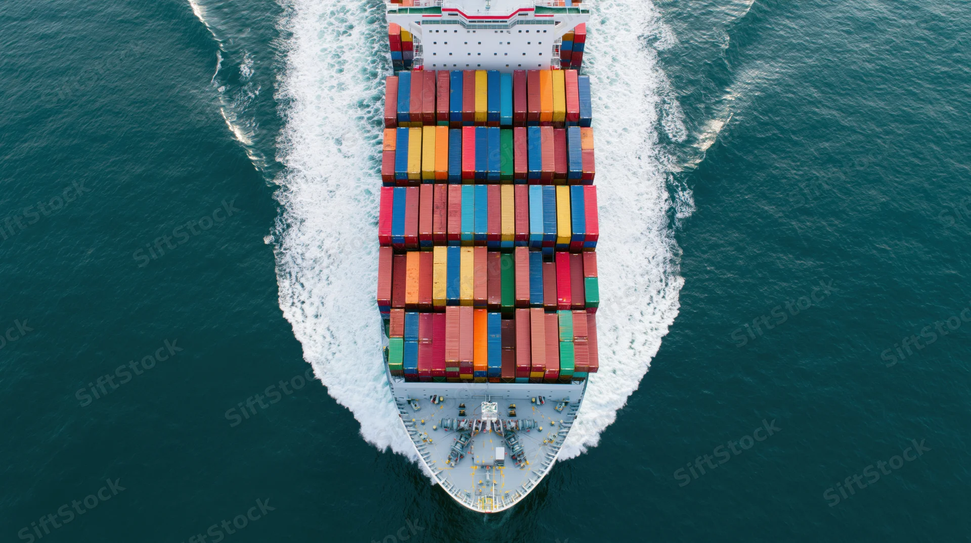 Overhead view of a large cargo container ship moving through the ocean with multicolored containers stacked on deck