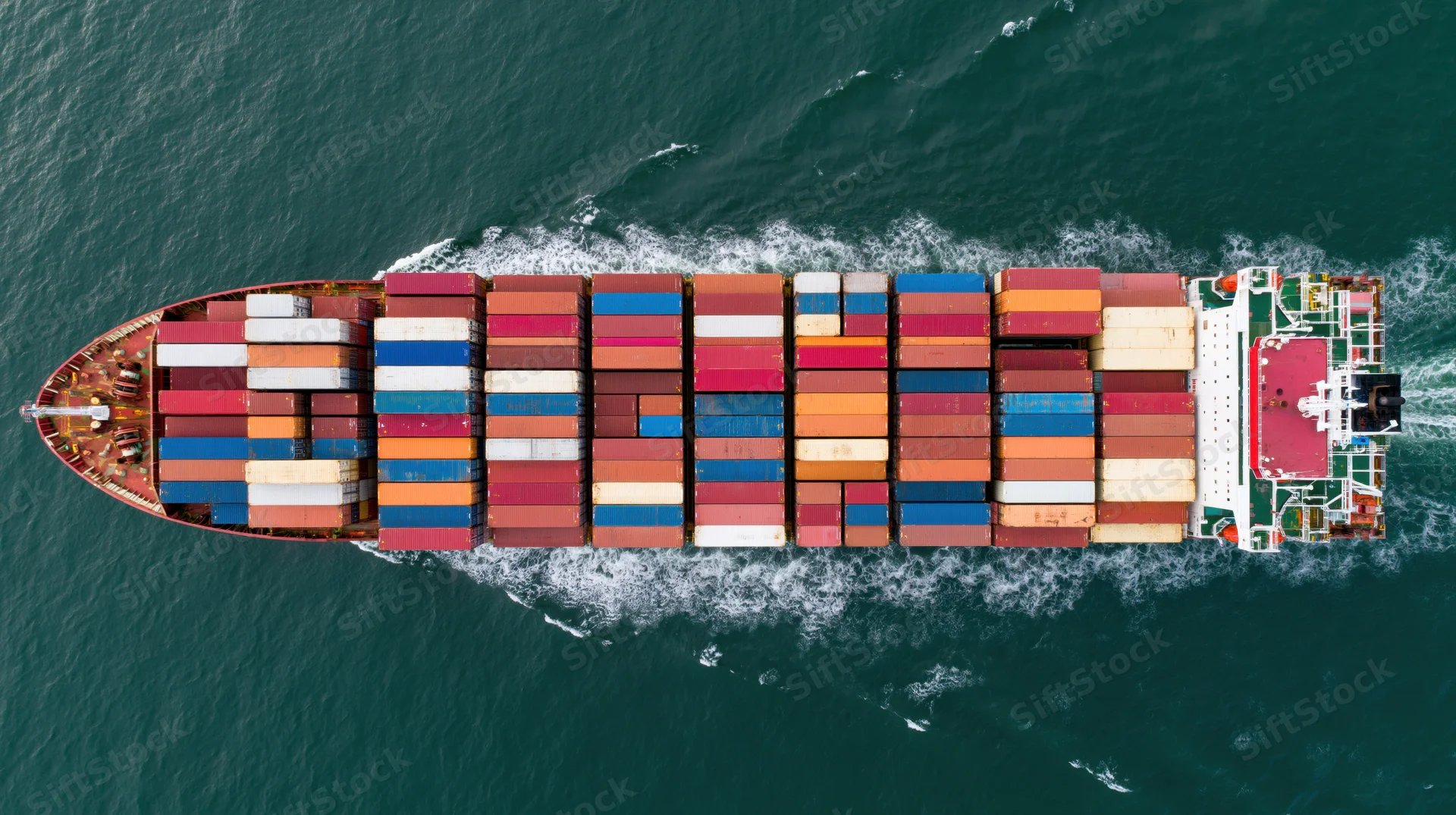 Overhead view of a large container ship loaded with stacked multicolored cargo containers sailing on the ocean