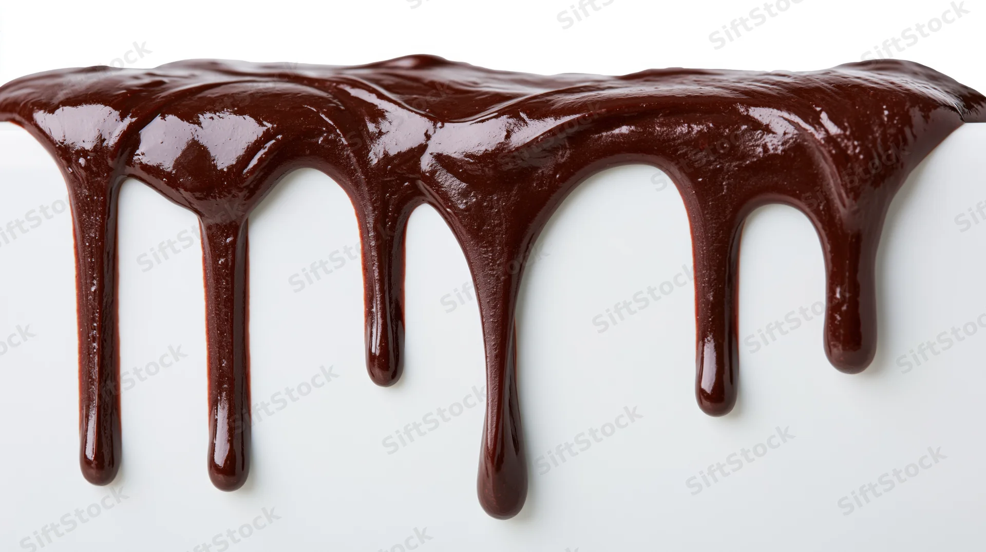 Melted dark chocolate dripping in thick glossy streams over white surface