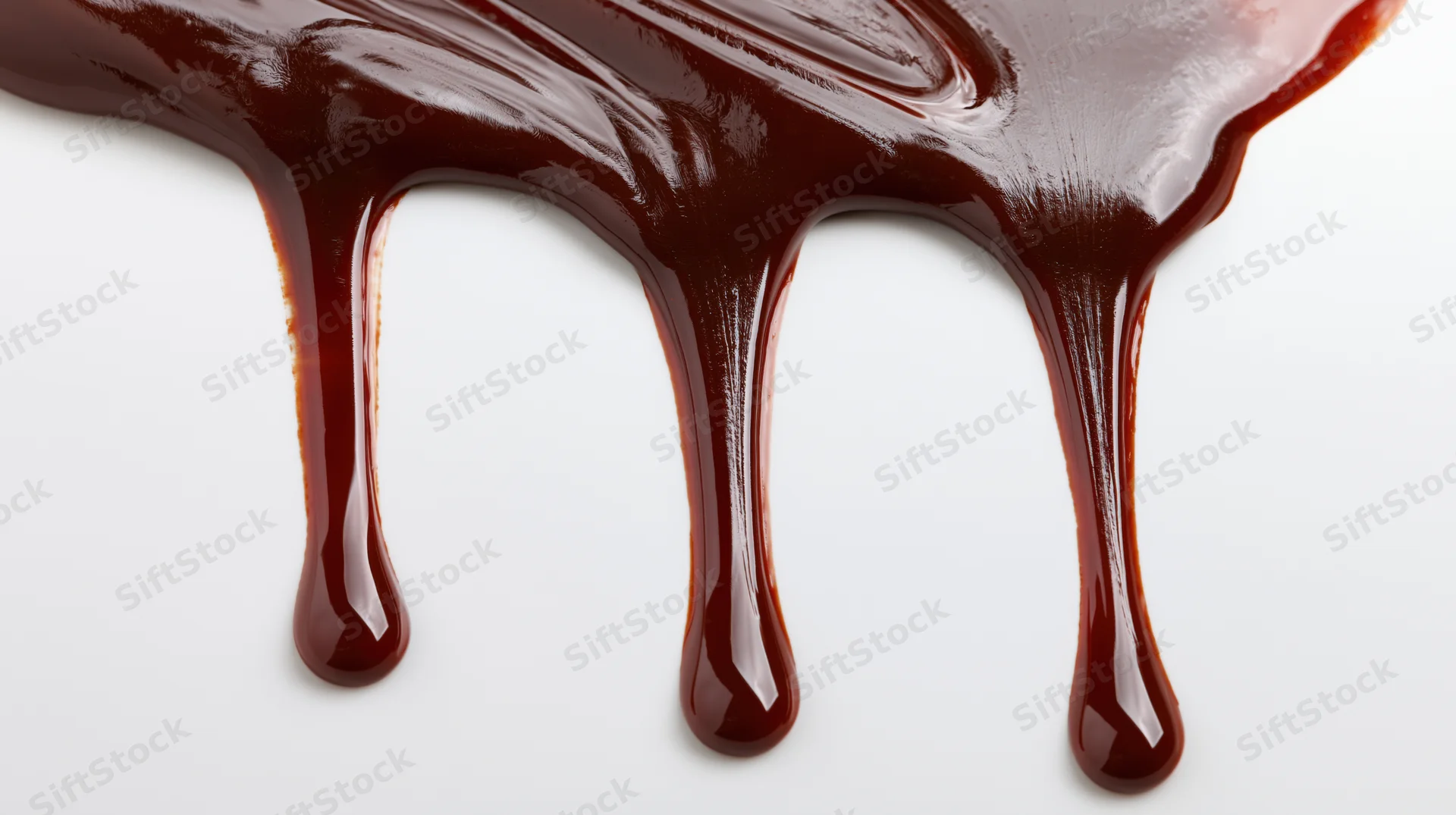 Melted dark chocolate dripping in slow streams on a white surface