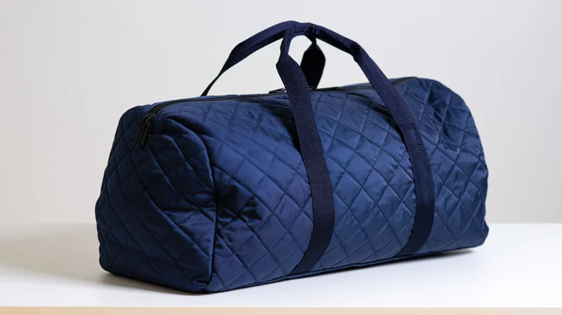 Navy blue quilted nylon duffel bag with handles sitting on white surface