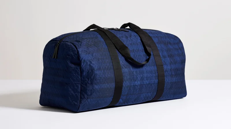 Navy blue nylon duffel bag with black straps sitting upright on a white surface