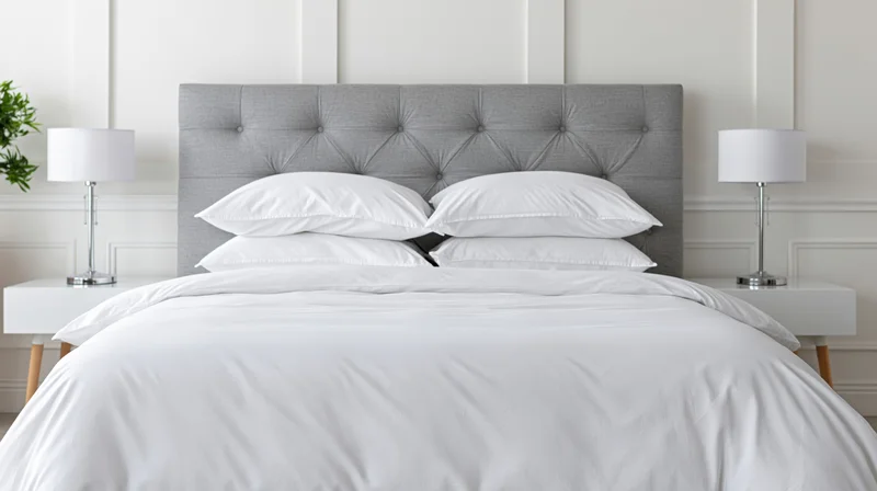 Neatly made bed with white bedding and gray tufted headboard in a modern bedroom