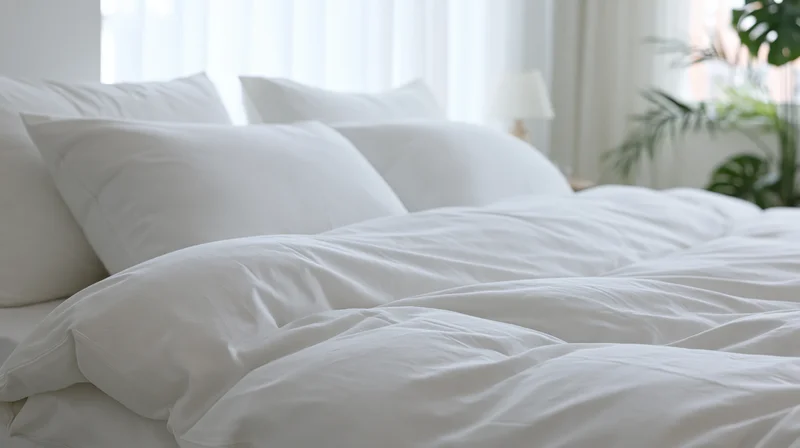 Neatly made hotel bed with crisp white pillows and duvet in a bright bedroom with plants and window light