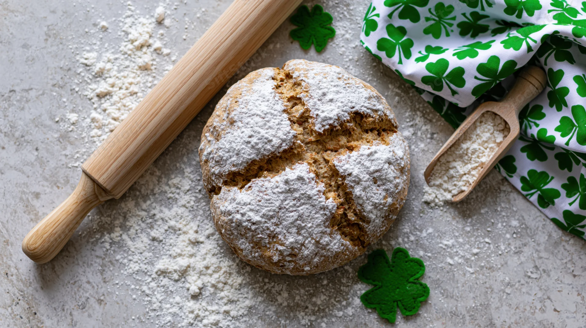 Round rustic irish soda bread dusted with flour on countertop with rolling pin and shamrock cloth