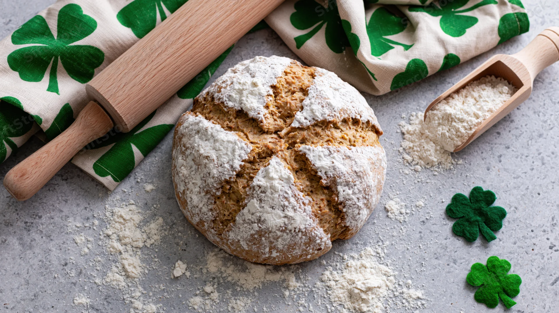 Round rustic irish soda bread dusted with flour on a countertop with clover decorations and baking tools
