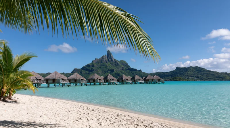 Overwater thatched-roof bungalows on a tropical beach with turquoise water and palm trees under a blue sky