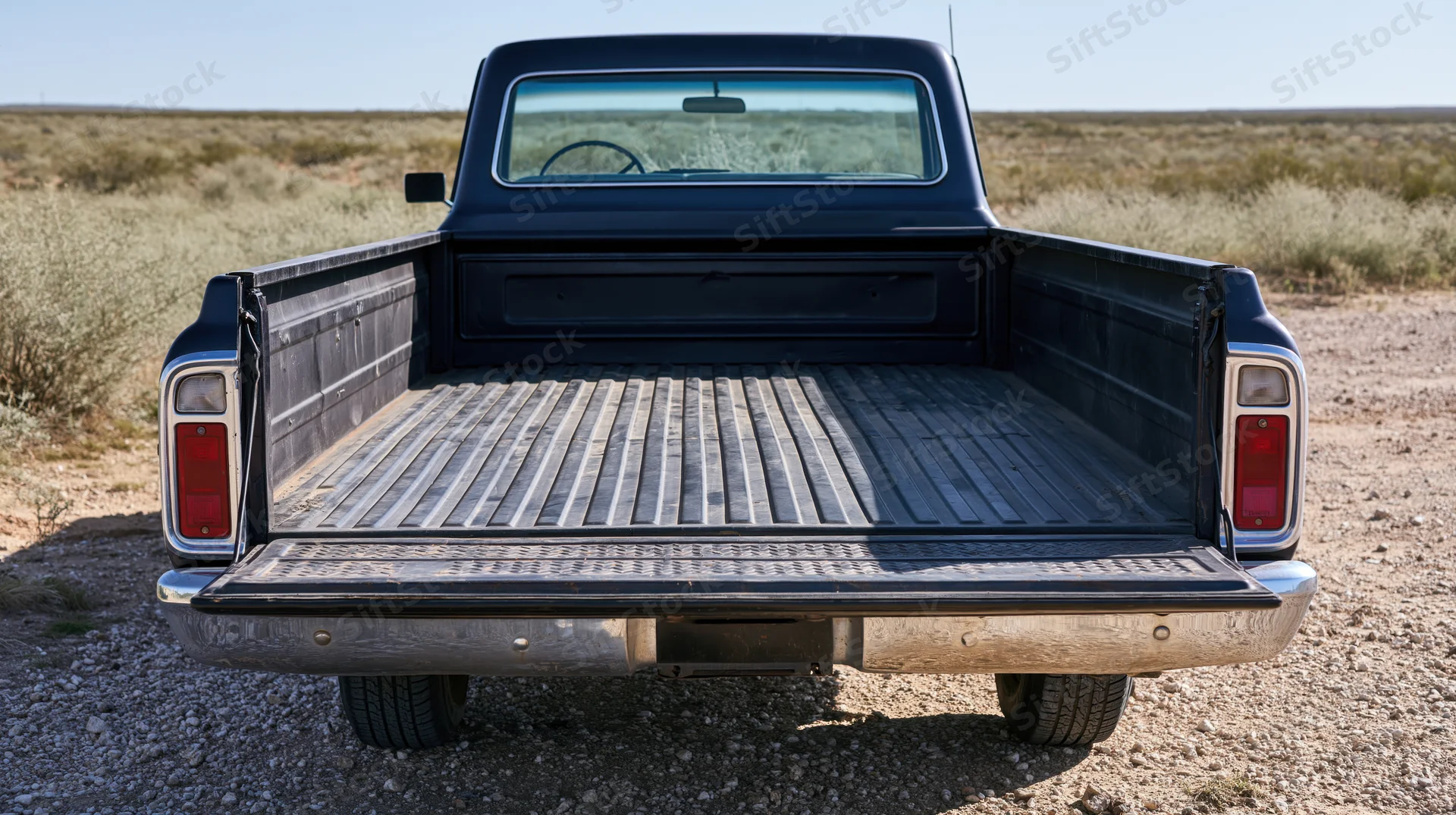 Rear view of a classic dark navy pickup truck with empty bed parked on gravel in a desert landscape
