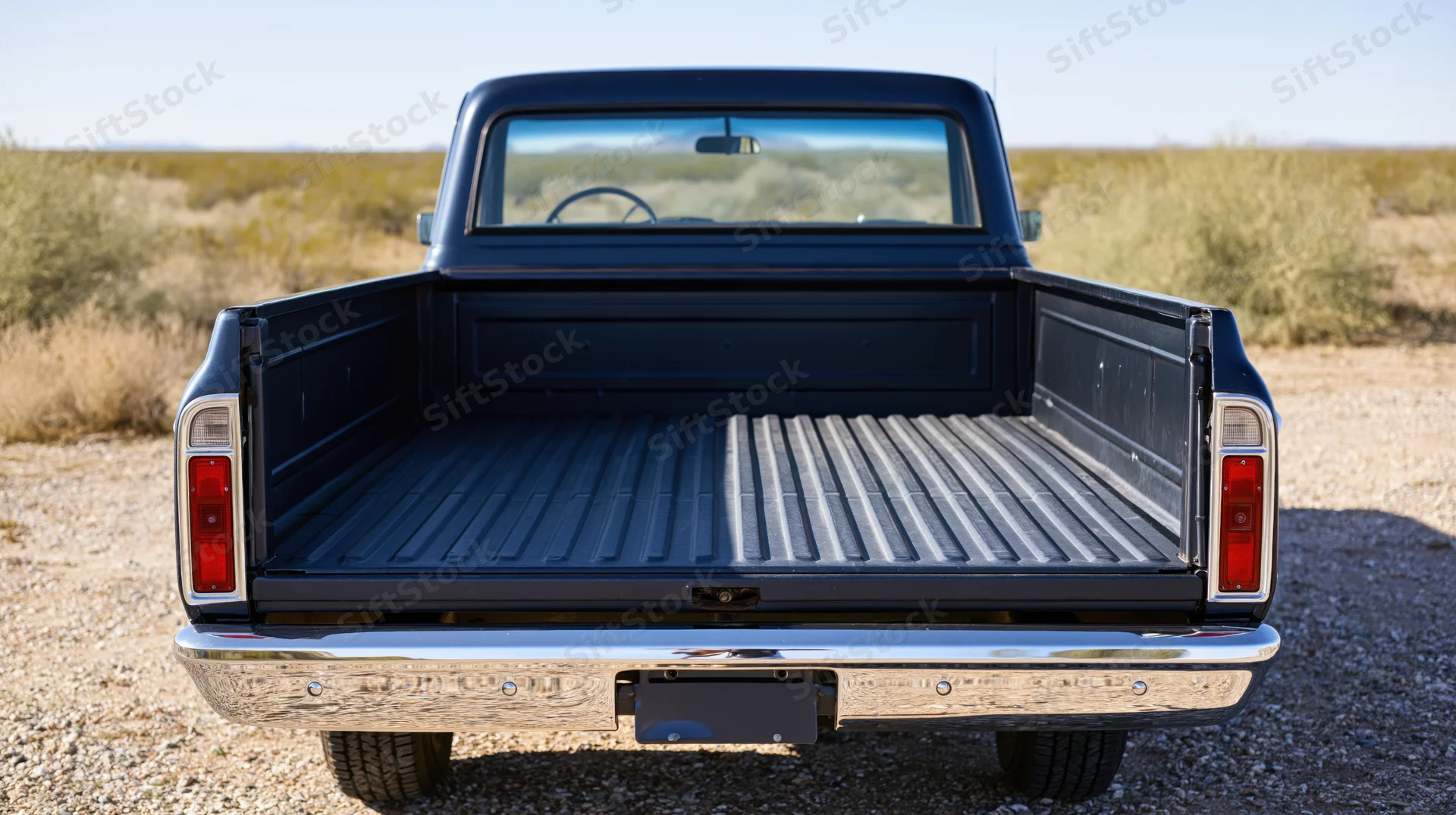 Rear view of a classic dark navy pickup truck with open tailgate and empty bed in a desert landscape