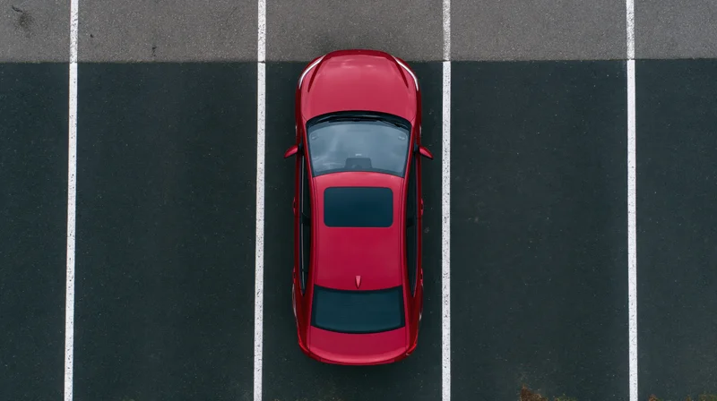 Red sedan parked alone in empty lot viewed from directly above