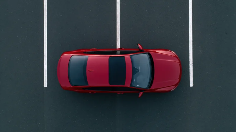 Red sedan parked alone in an empty parking lot viewed from directly above