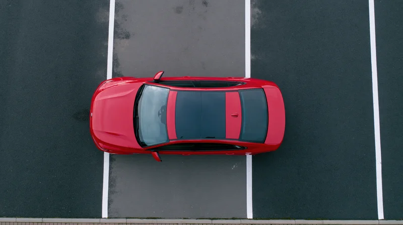 Red sedan parked alone in an empty parking lot viewed from directly above