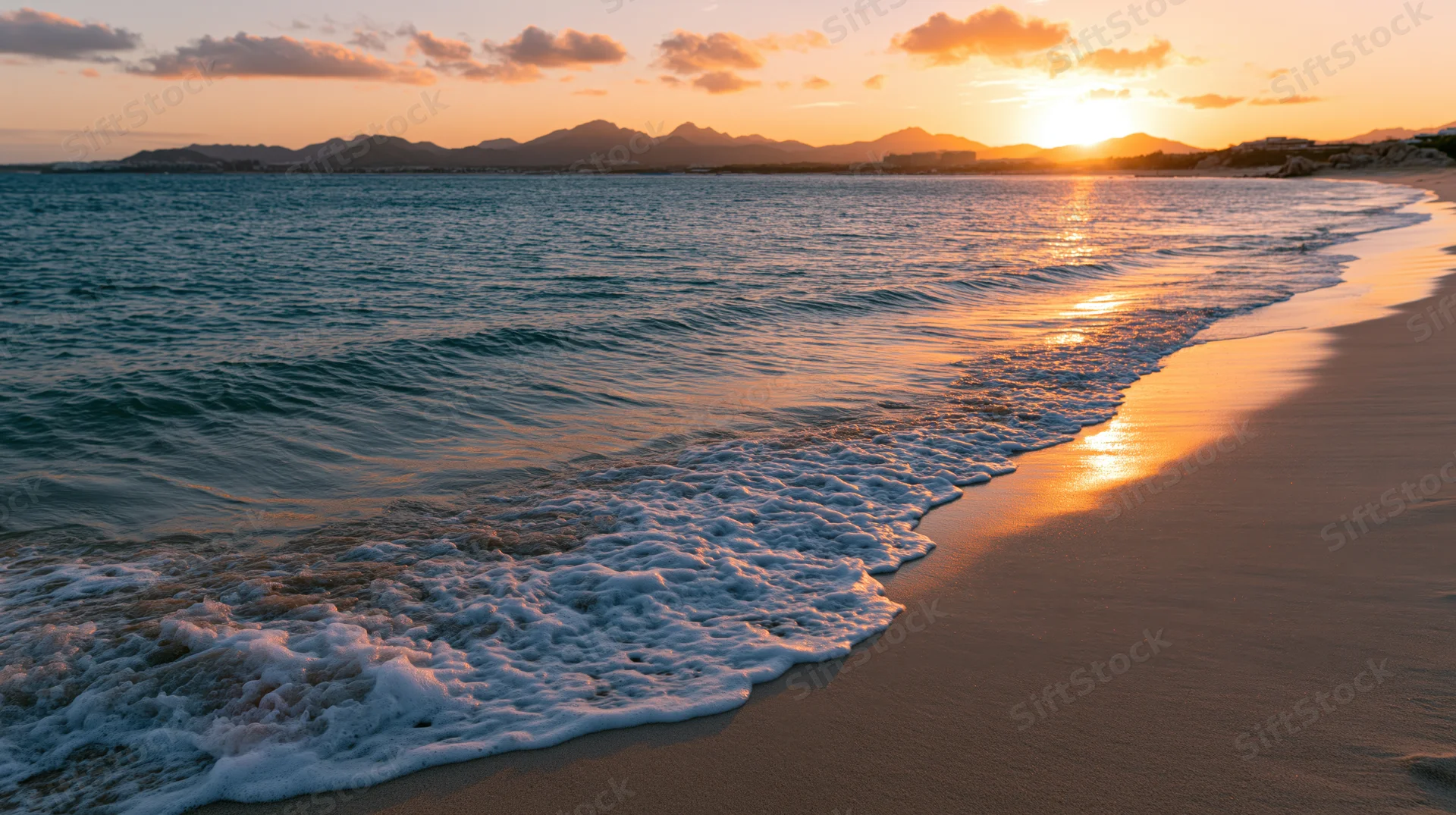 Gentle foamy wave rolling onto sandy beach at sunset with distant mountains on the horizon