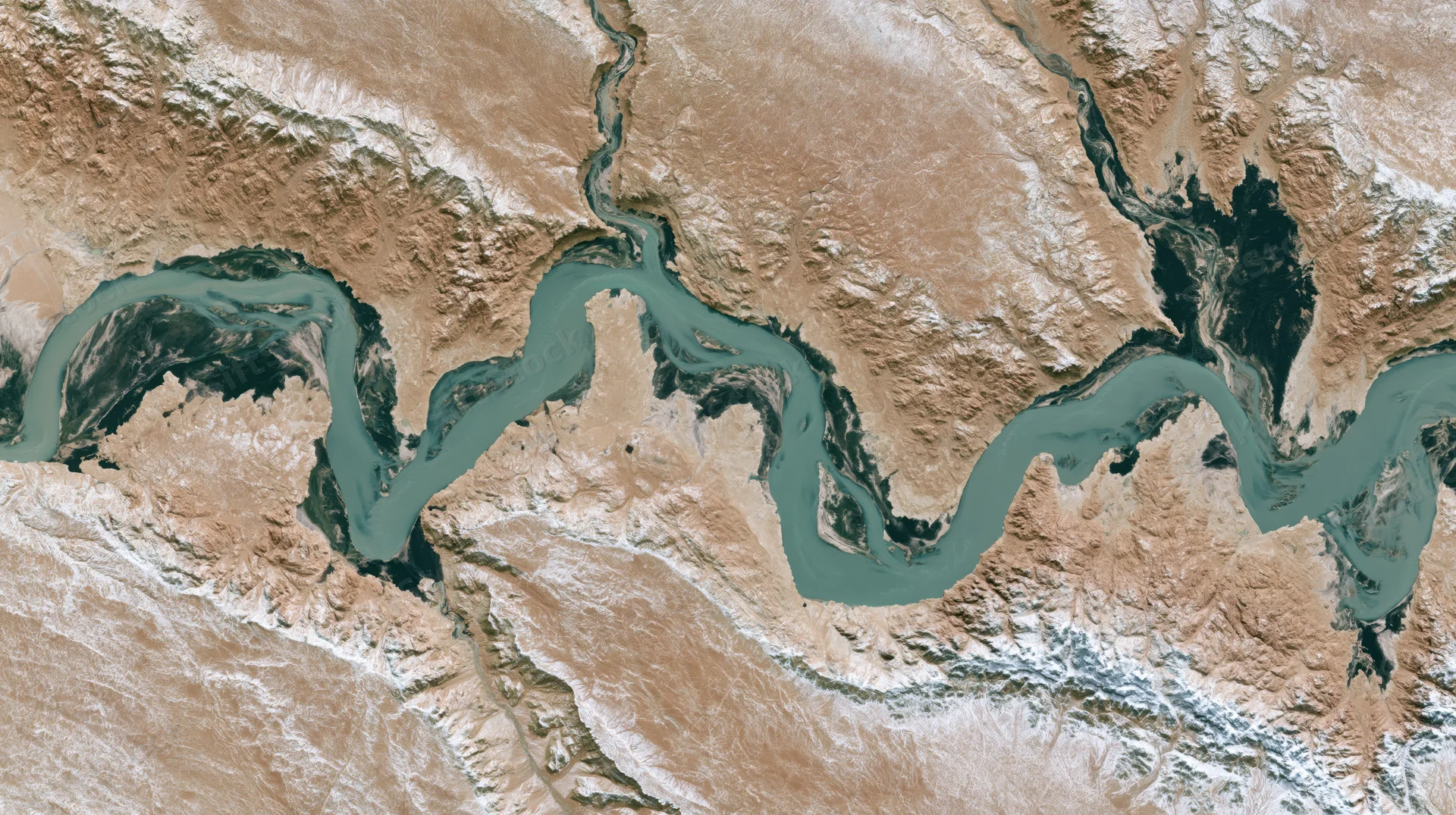 Satellite view of a winding river delta flowing through arid desert terrain with snow-covered mountains