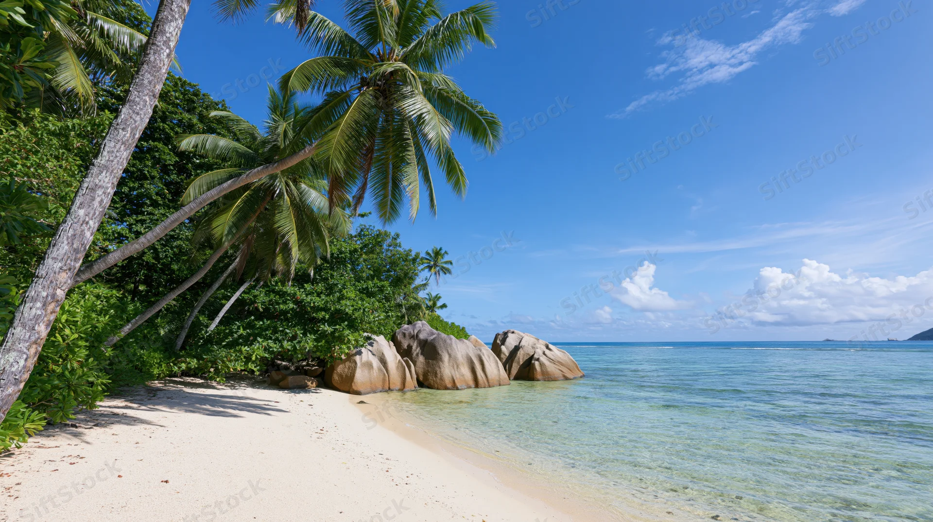 Secluded tropical beach with white sand curving toward large rocks and palm trees under a clear blue sky