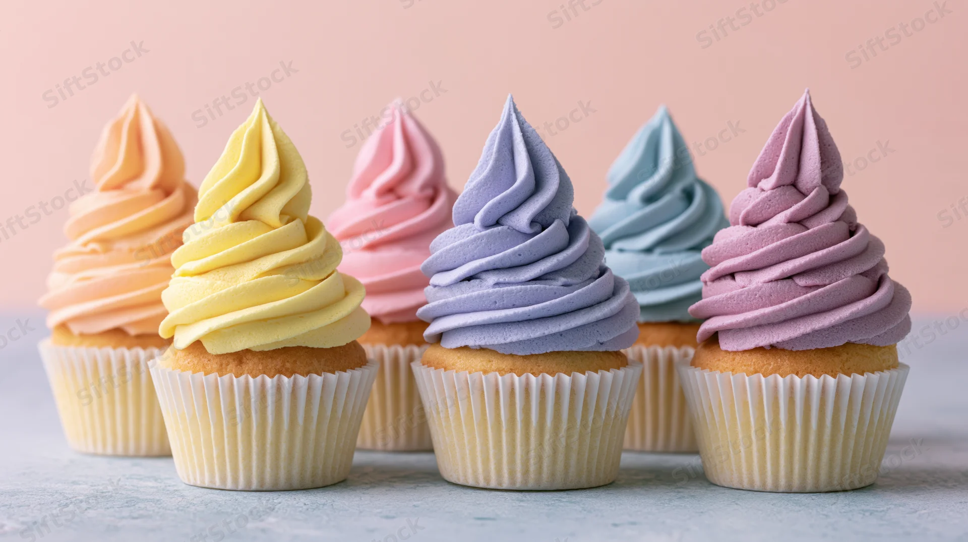 Six cupcakes with pastel frosting arranged in a row on a light gray surface