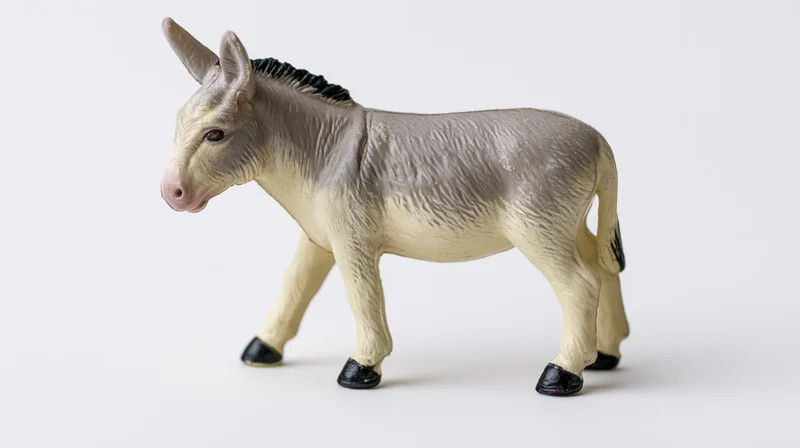 Small plastic donkey figurine standing in profile view on white background