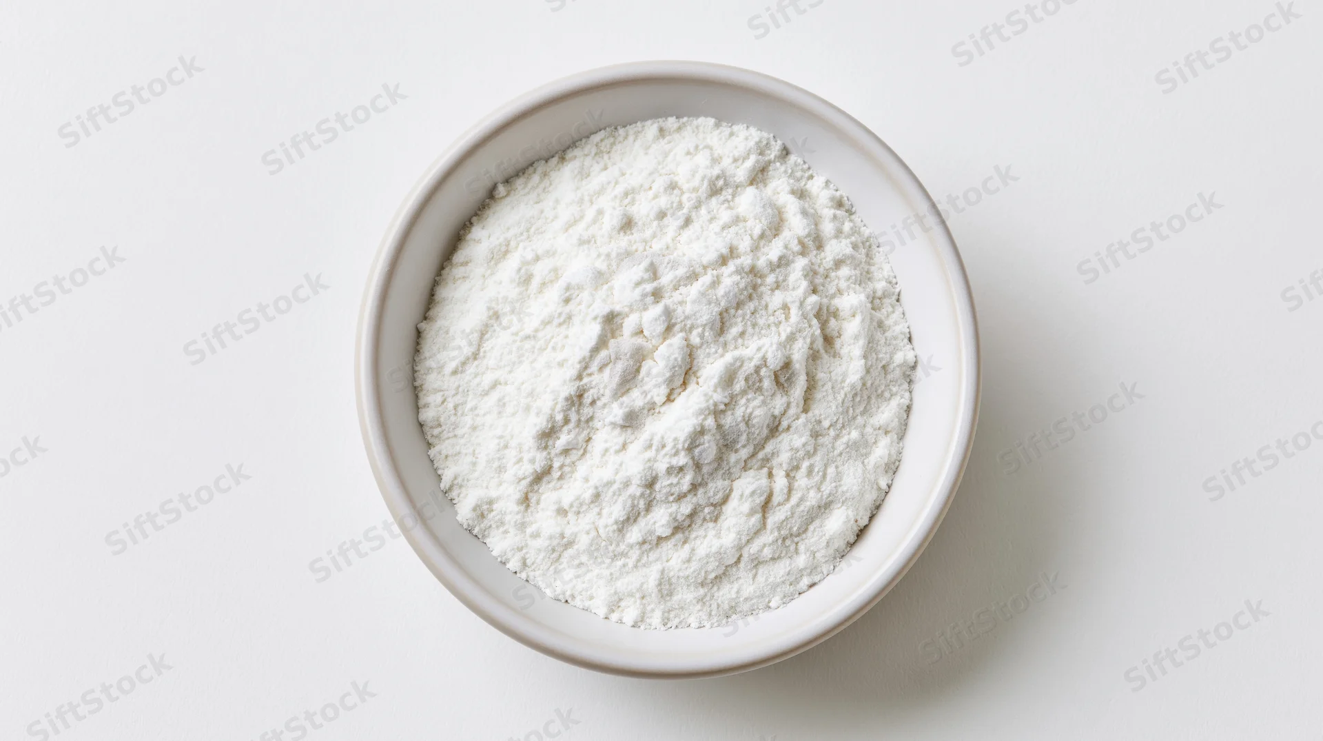 White ceramic bowl filled with fine white flour on plain white surface, overhead view