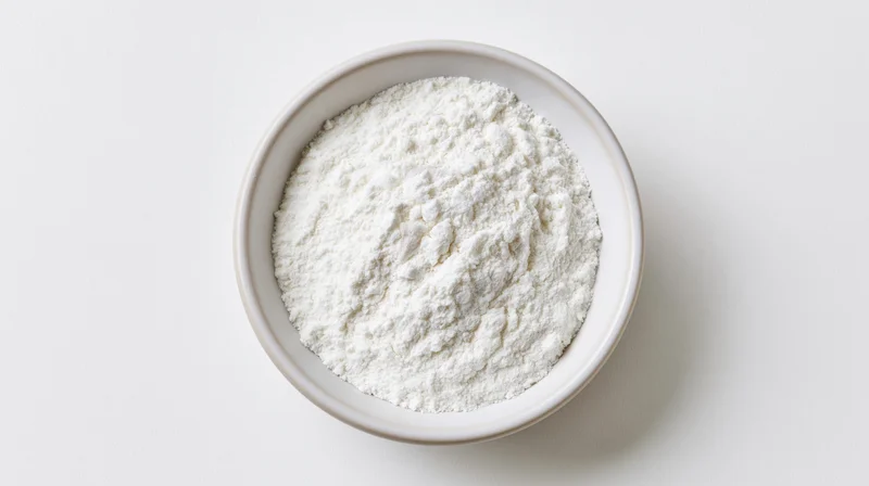 White ceramic bowl filled with fine white flour on plain white surface, overhead view