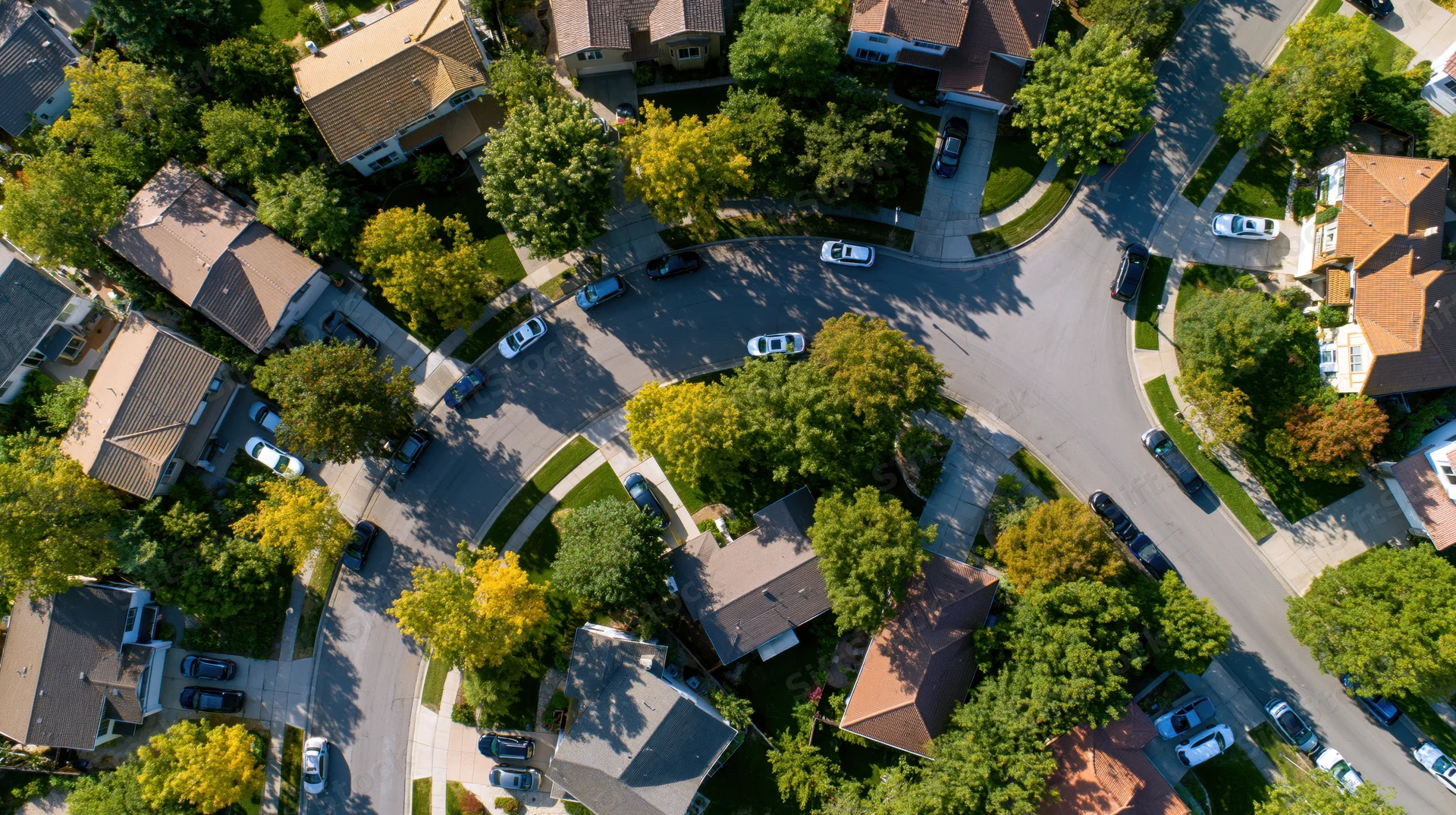 Aerial view of a suburban neighborhood with houses, trees, and parked cars arranged along curving streets