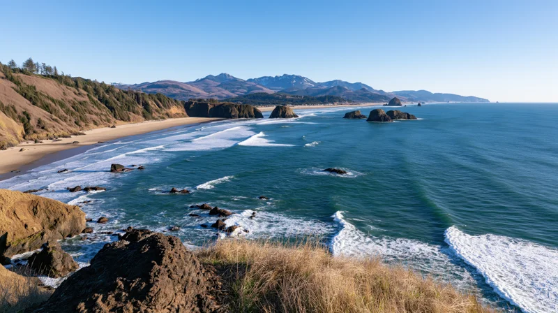 Sweeping view of a curved pacific northwest coastline with waves breaking on sandy beach and rocky cliffs under clear blue sky