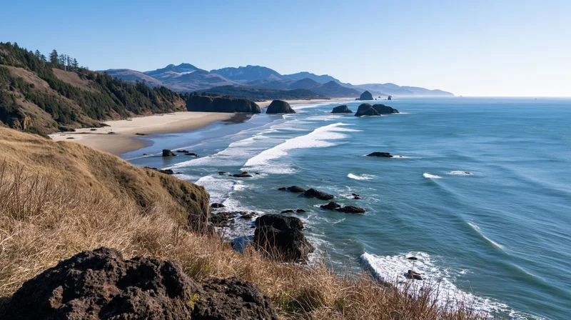 Sweeping view of a curved pacific northwest coastline with waves breaking on sandy beach and rocky cliffs under clear blue sky