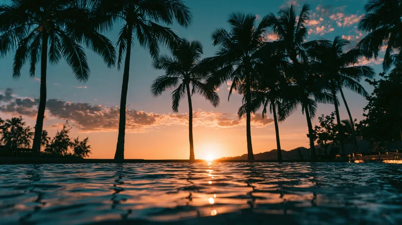 Silhouetted palm trees framing a tropical sunset over calm ocean water