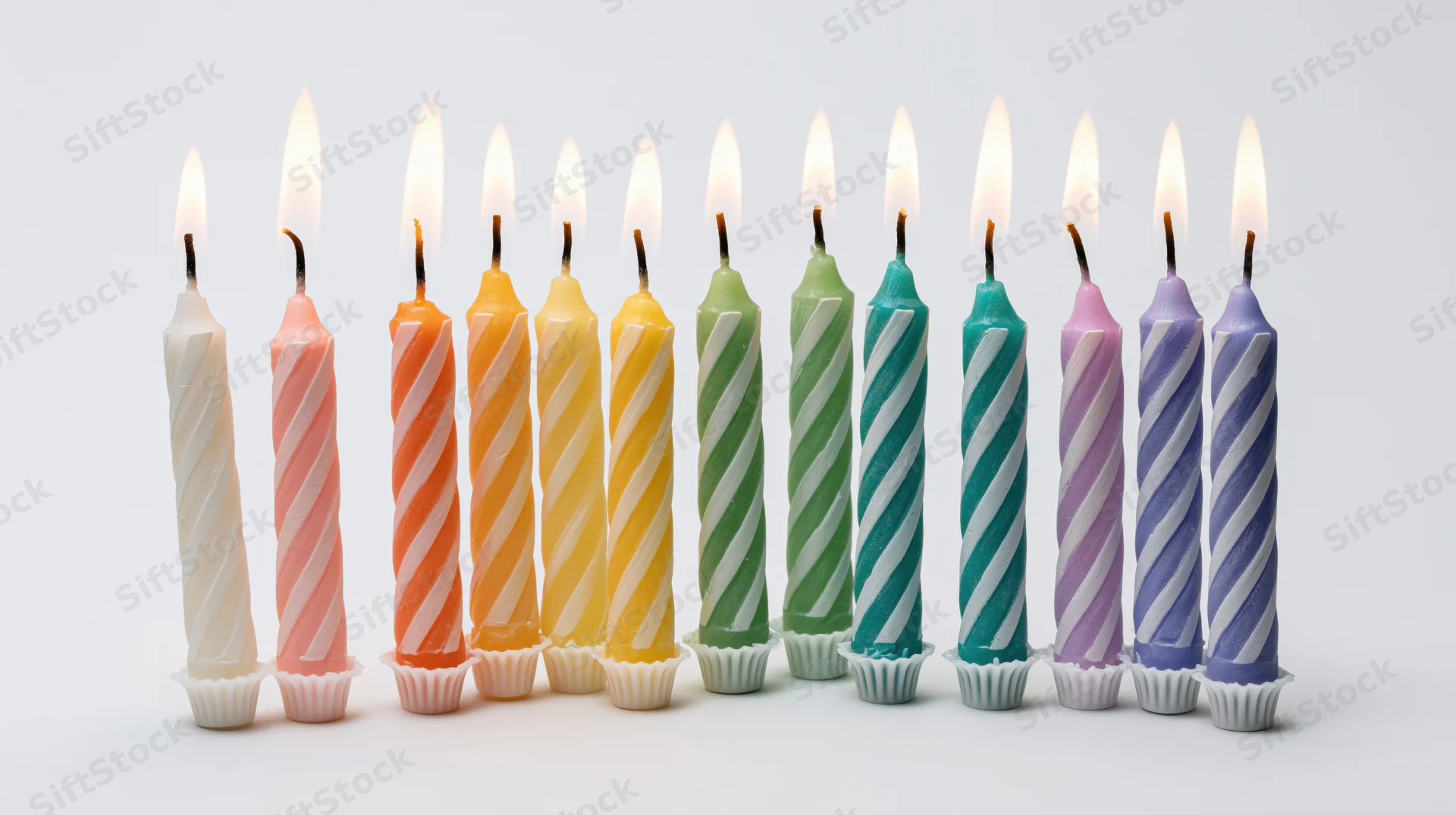 Ten lit birthday candles in a rainbow row on a white background