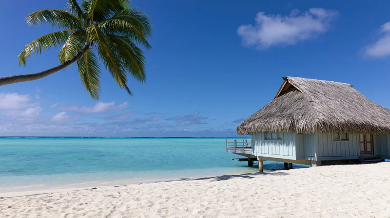 Thatched-roof bungalow on stilts over turquoise water at tropical beach with palm tree and blue sky