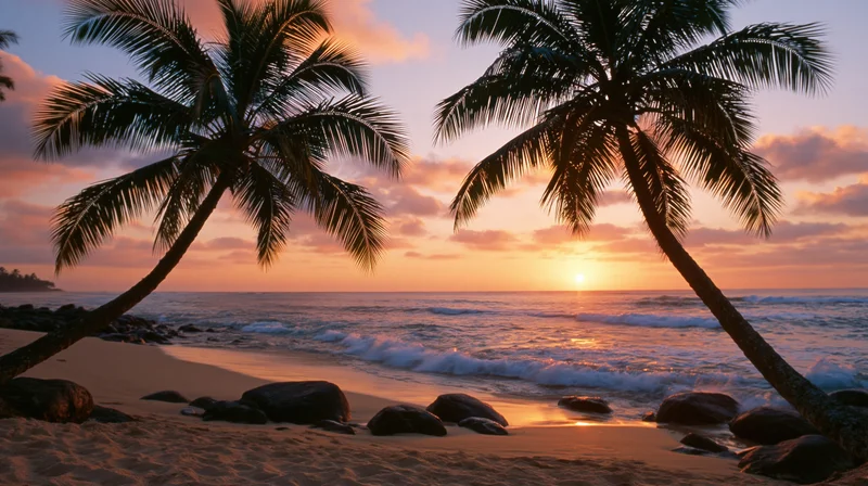 Tropical beach at sunset framed by two leaning coconut palms with waves and rocks on the shore
