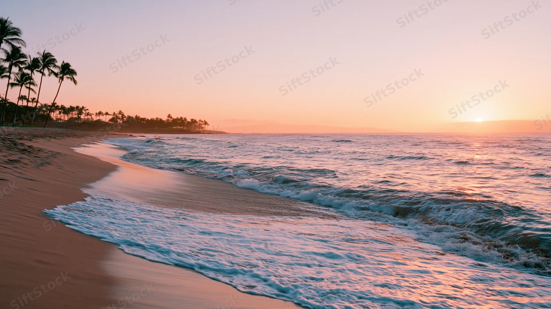 Gentle waves washing onto a sandy beach at sunset with palm trees along the shore