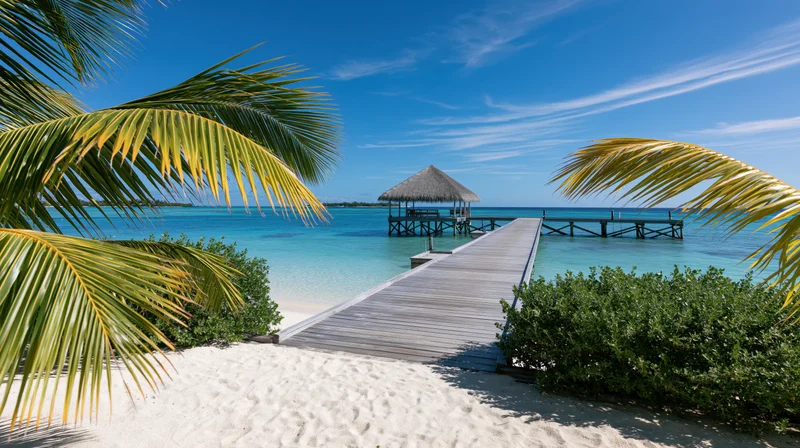 Wooden pier extending over shallow turquoise water to a thatched hut on a tropical beach