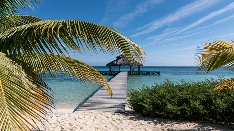 Wooden pier extending over turquoise ocean to thatched hut on tropical beach
