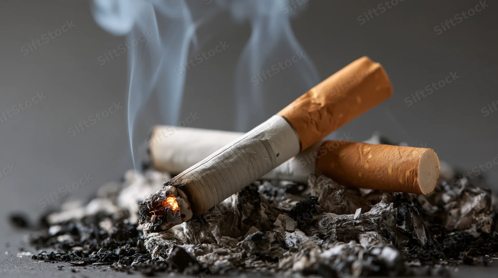 Smoldering cigarette butts resting in a pile of ash with rising smoke