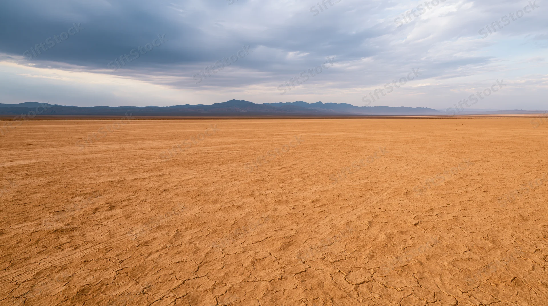 Vast cracked desert plain stretching toward distant mountains under cloudy sky