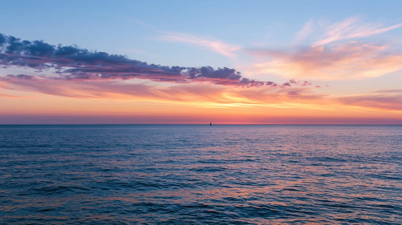 Vast ocean at sunset with a single sailboat silhouetted on the horizon