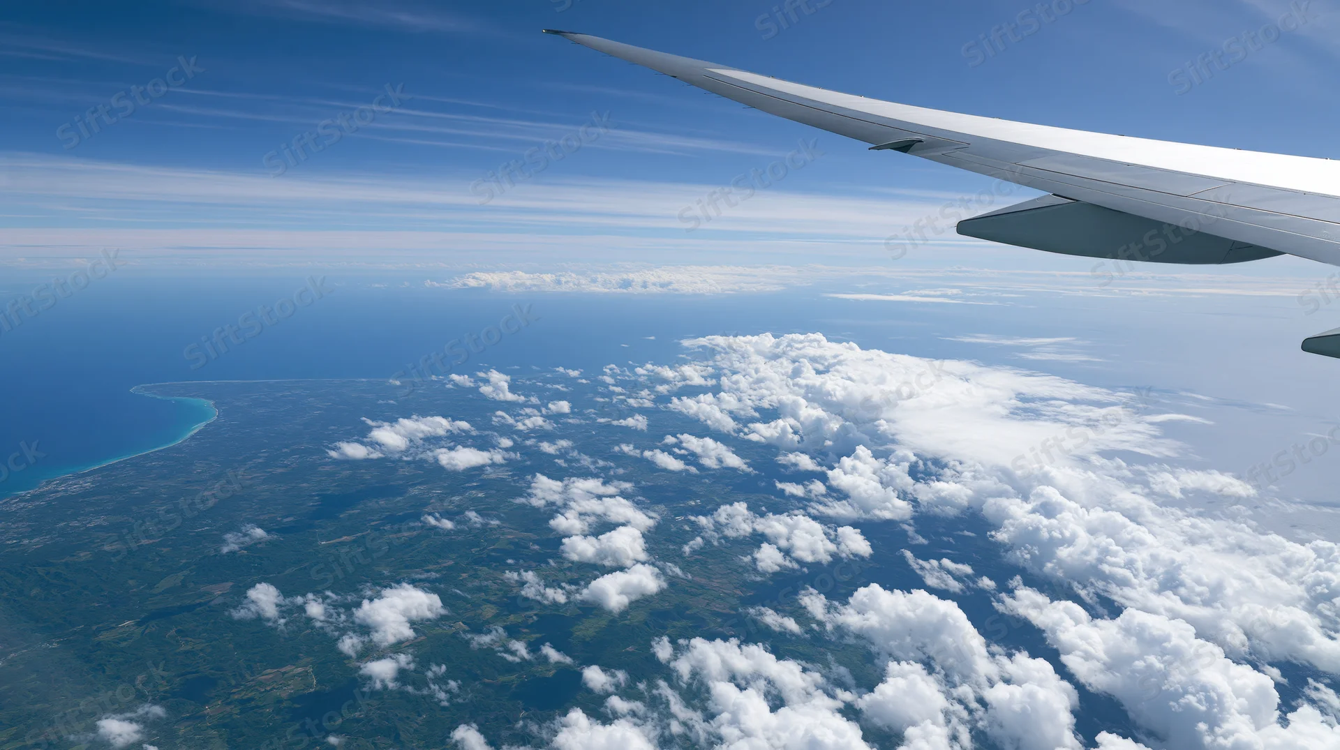 Airplane wing extending over clouds and coastline from high altitude view