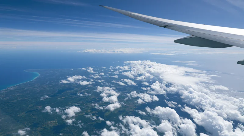 Airplane wing extending over clouds and coastline from high altitude view