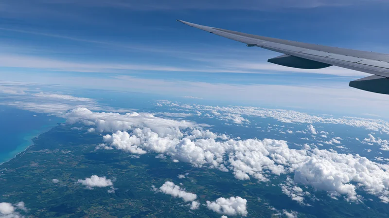 Airplane wing extending over clouds and coastline from high altitude aerial view