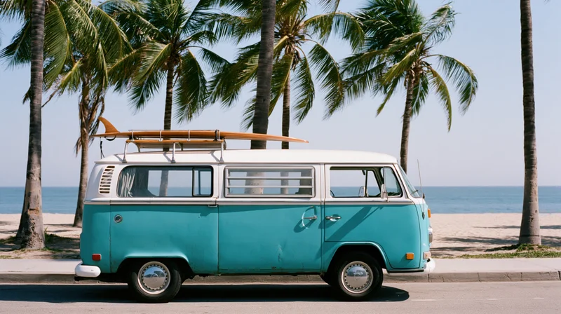 Vintage turquoise and white volkswagen camper van parked on beachside road with surfboard on roof rack near palm trees and ocean