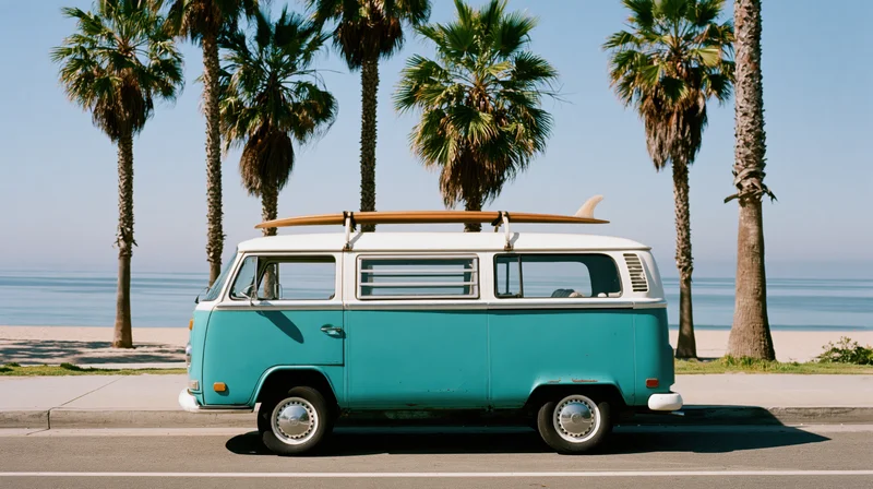 Vintage turquoise and white volkswagen camper van parked on coastal road beside beach with palm trees and surfboard on roof