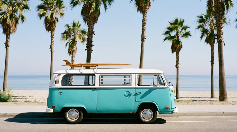 Vintage turquoise and white volkswagen camper van parked on beachside road with surfboard on roof rack near palm trees and ocean