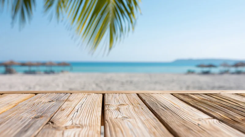 Weathered wooden deck table in foreground overlooking sandy beach and turquoise ocean under palm fronds