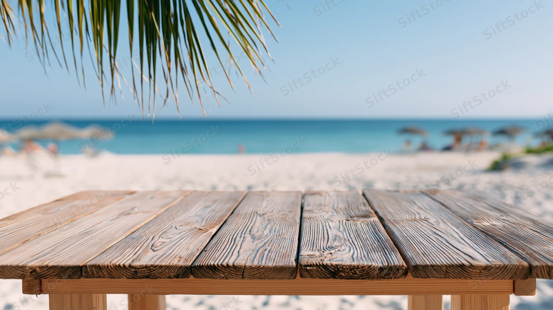 Weathered wooden table on a sandy beach overlooking the ocean under palm fronds