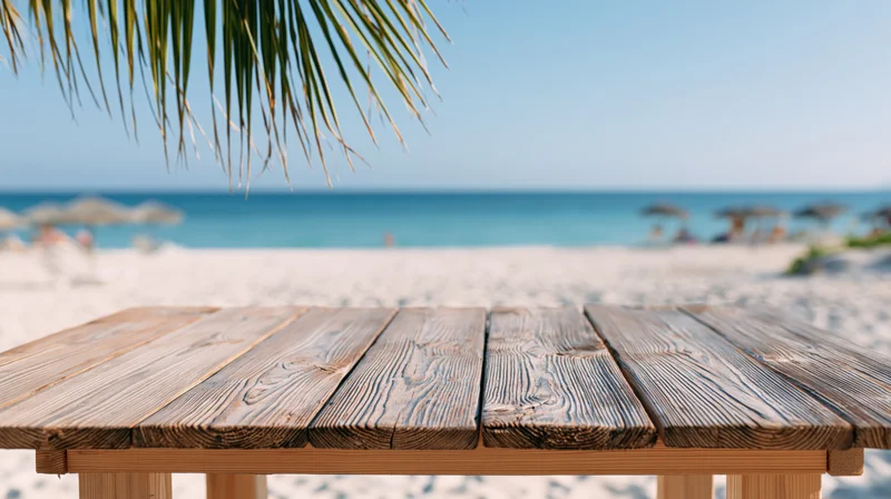 Weathered wooden table on a sandy beach overlooking the ocean under palm fronds