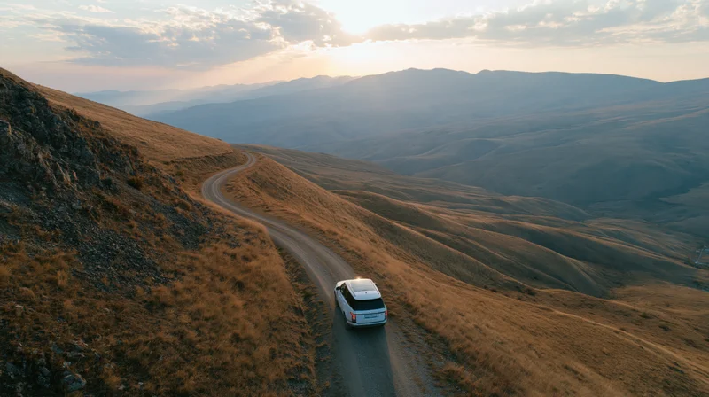 White suv driving on winding gravel road through mountainous landscape at sunset