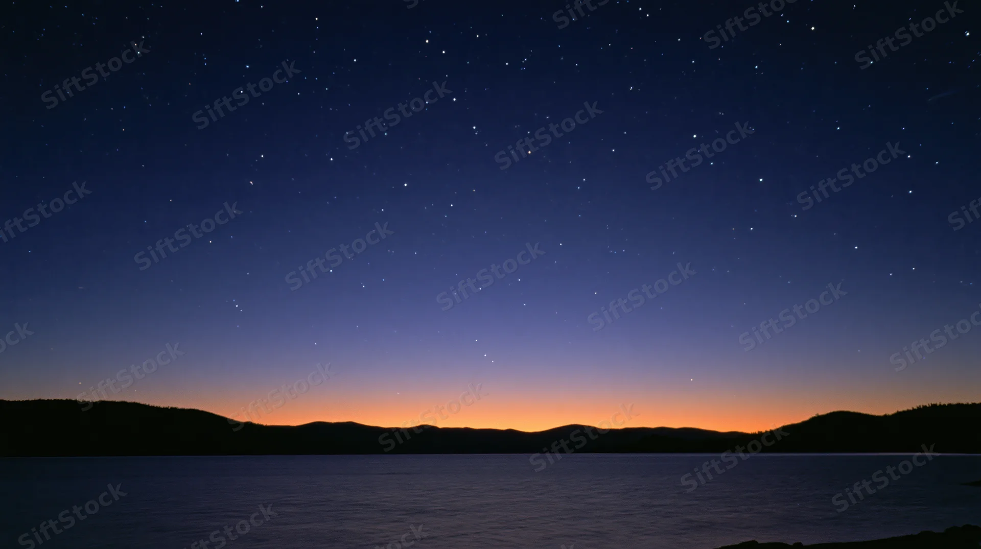 Starry night sky over calm lake with distant mountains at twilight